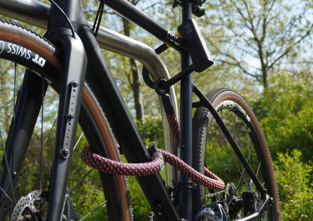 Fiets vastgemaakt aan het achterwiel, voorwiel en fietsframe met D-slot U-slot en eyelet textieltouw in chateau red op de fietsstandaard