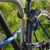 Fiets vastgemaakt aan het achterwiel, voorwiel en fietsframe met D-slot U-slot en eyelet textieltouw in morpho blue op de fietsstandaard