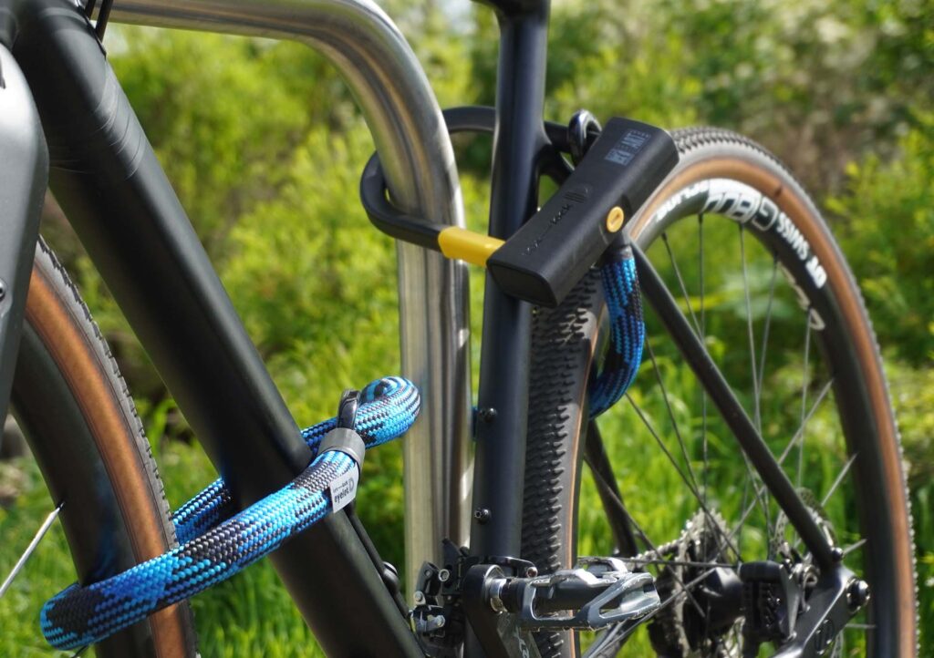 Fiets vastgemaakt aan het achterwiel, voorwiel en fietsframe met D-slot U-slot en eyelet textieltouw in morpho blue op de fietsstandaard