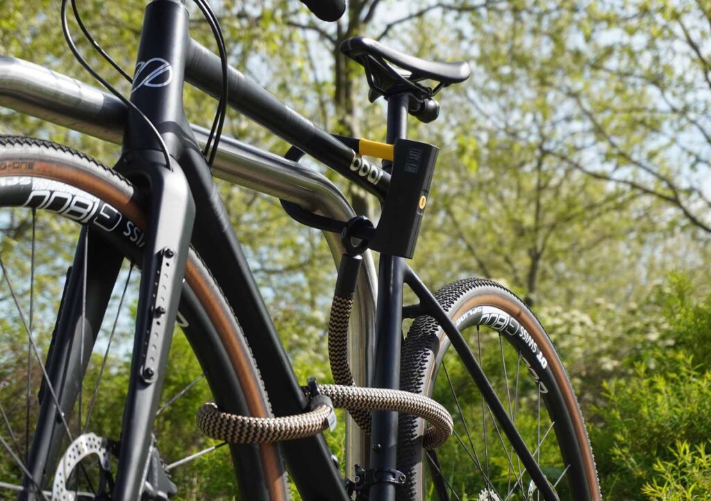 Fiets vastgemaakt aan het achterwiel, voorwiel en fietsframe met D-slot U-slot en eyelet textieltouw in wild hemp op de fietsstandaard