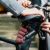 Model in een grijs colbert houdt fiets vast bij het zadel, met de tex-lock orbit in chateau red flexibel om de stuurstang gewikkeld