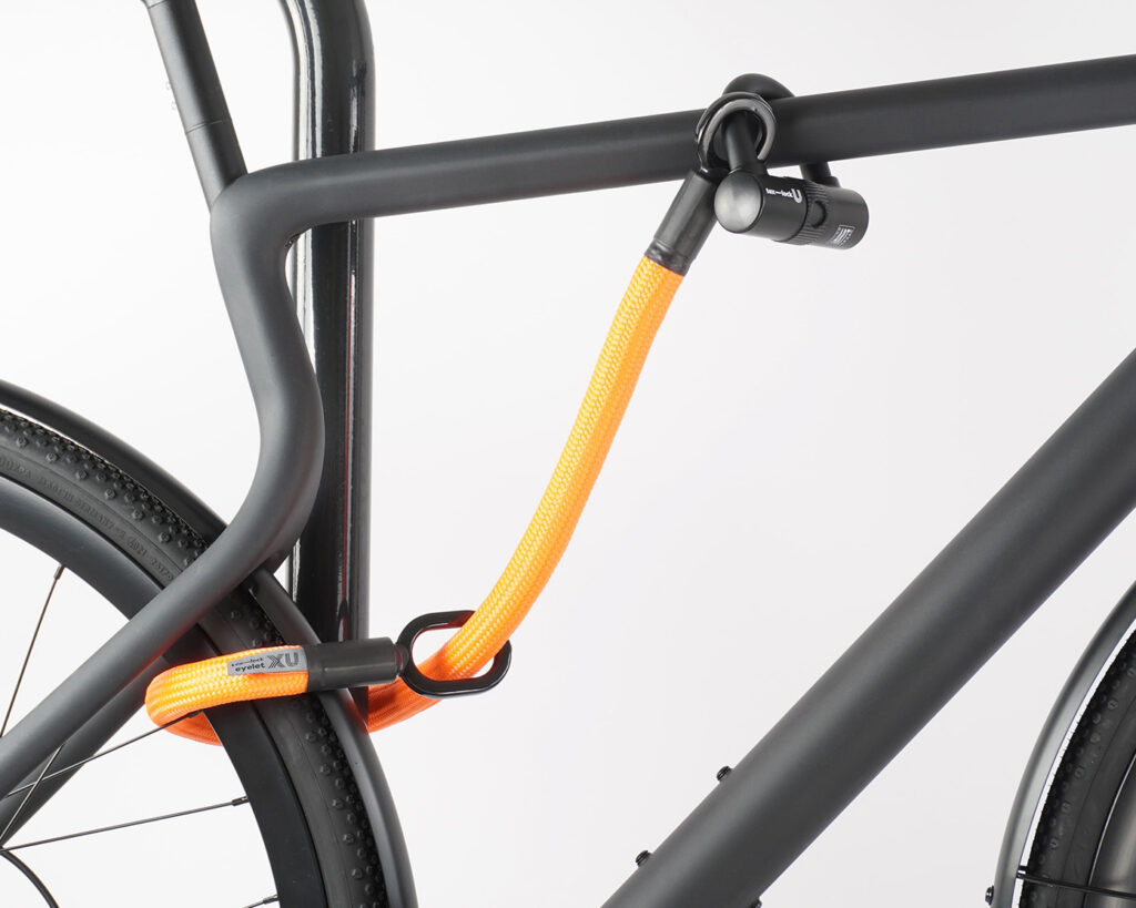 Rear wheel and top tube of the bike connected to the bike stand with U-lock and orange textile extension