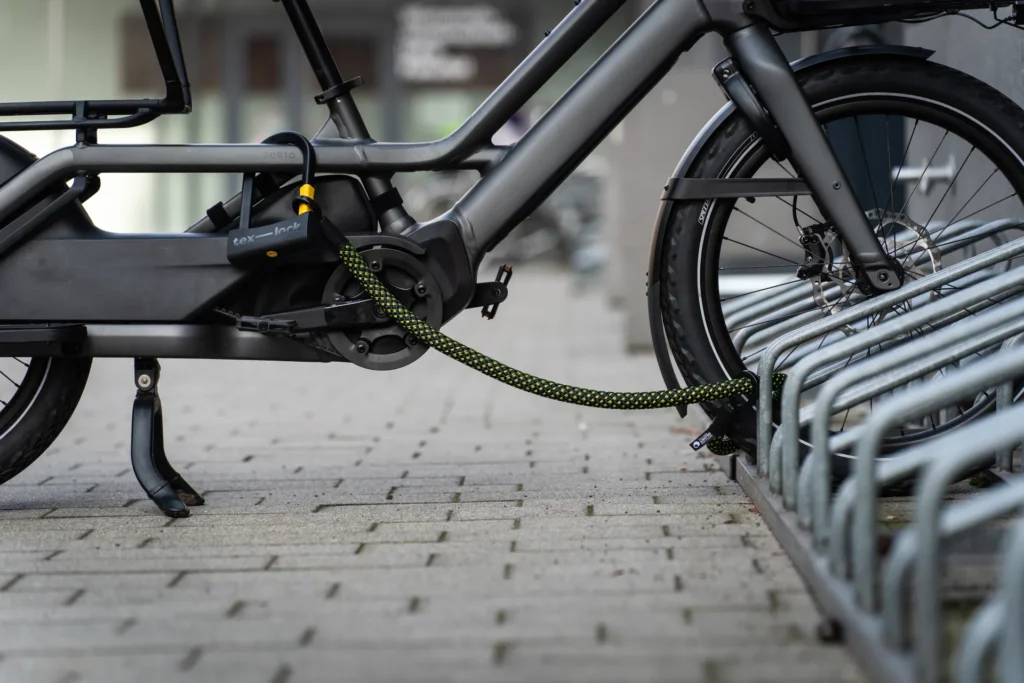 U-slot met textielkabel in zwart en neongeel patroon vergrendelt longtail fiets aan fietsenrek